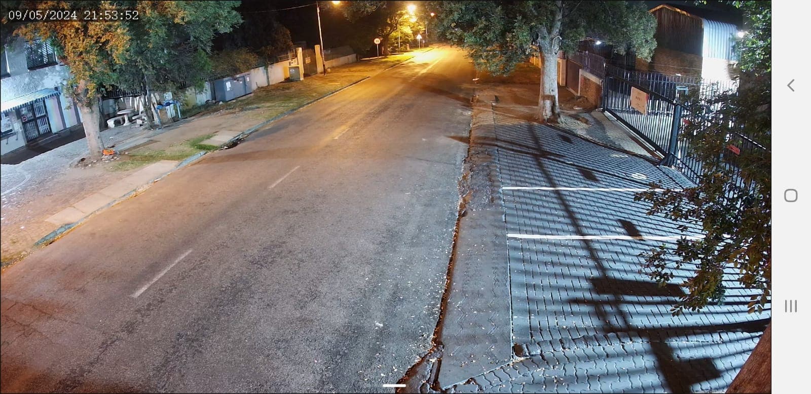 Empty residential street at night with streetlights illuminating the asphalt road and brick sidewalk.