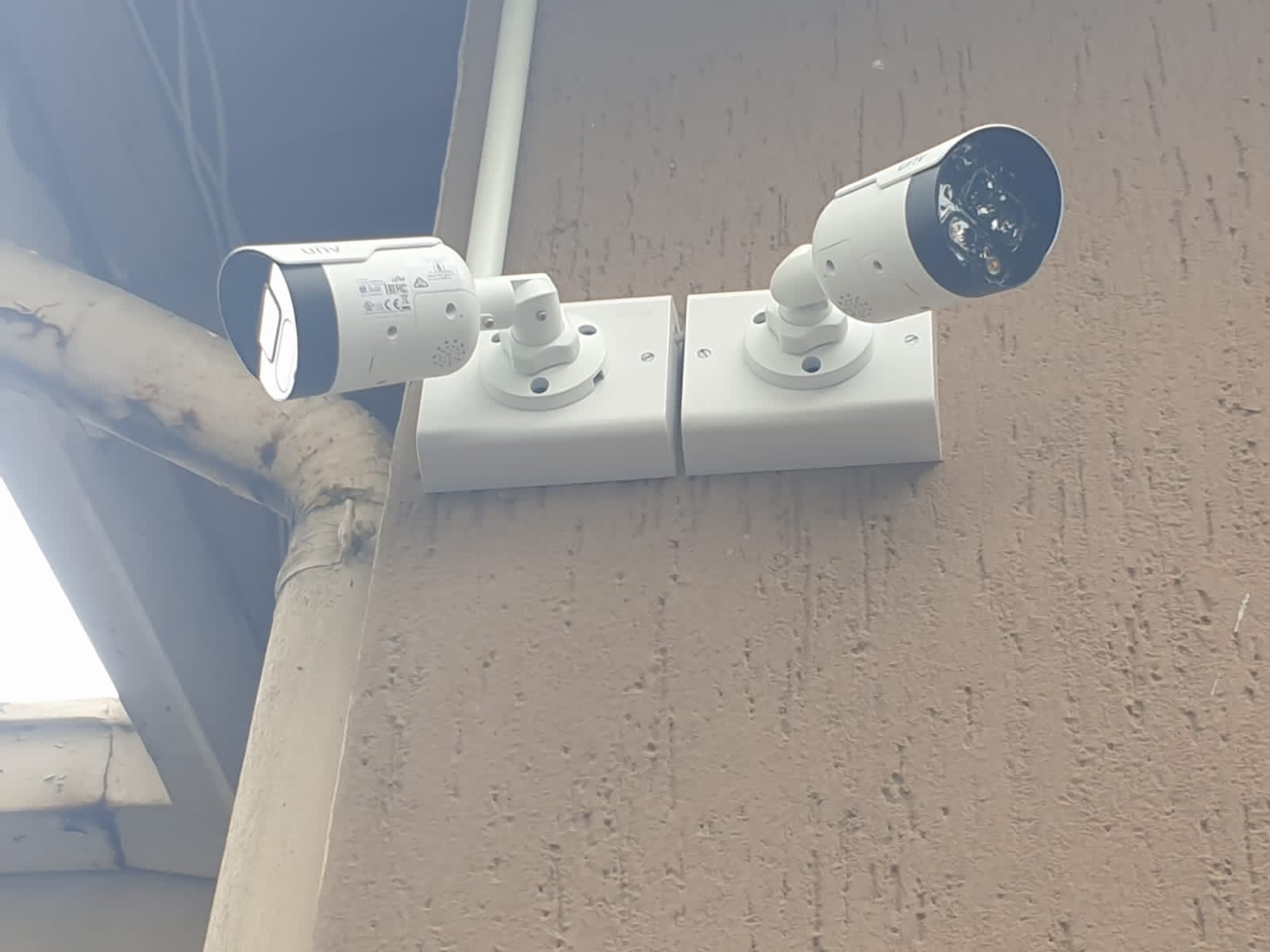 Two white bullet security cameras installed on a textured exterior wall, facing in opposite directions.