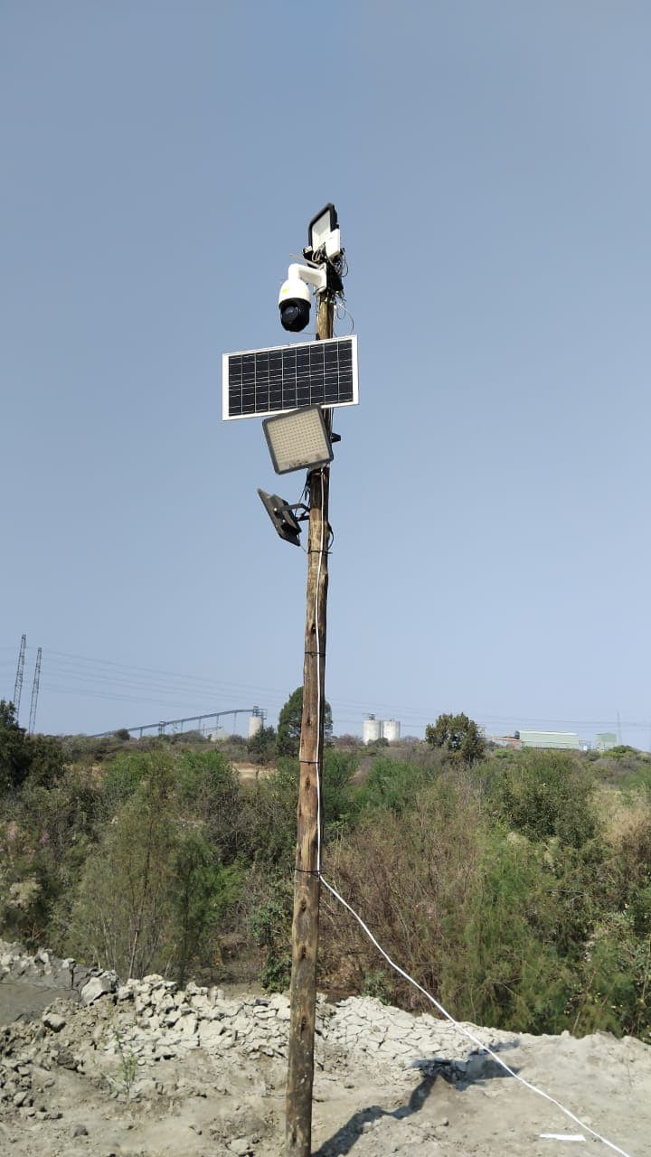 Solar-powered security camera and LED floodlights mounted on a tall wooden pole outdoors.