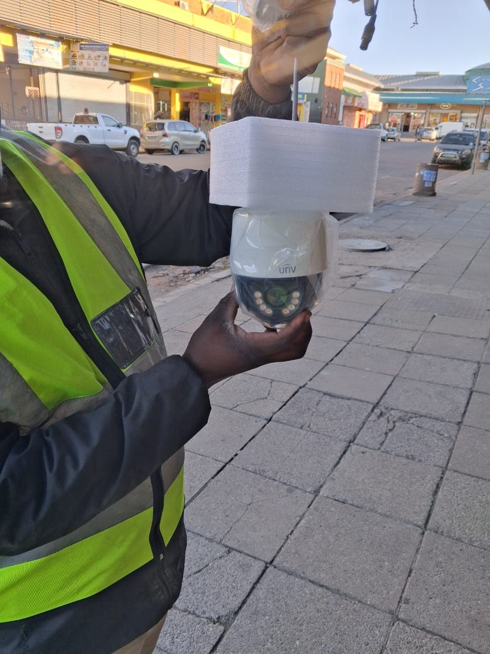 Worker in a safety vest holds a white UNV dome security camera on a sidewalk.