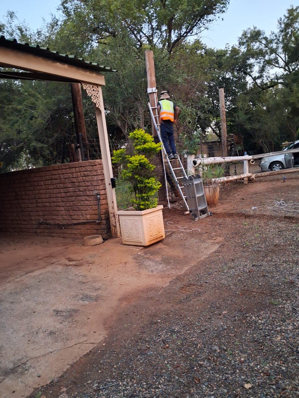 Worker in safety vest stands on a ladder leaning against a wooden pole.